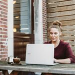 woman sitting and holding white Acer laptop near brown wooden wall
